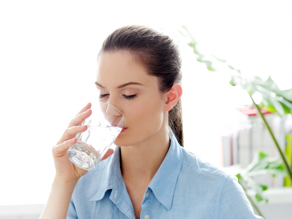 mujer tomando agua en vaso de vidrio con ojos cerrados