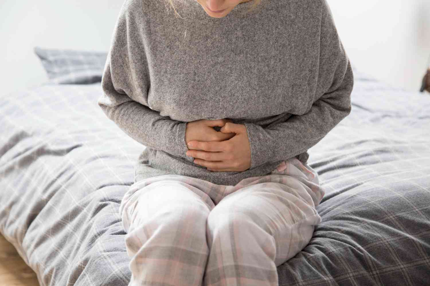 mujer sentada en borde de la cama con manos sobre el abdomen