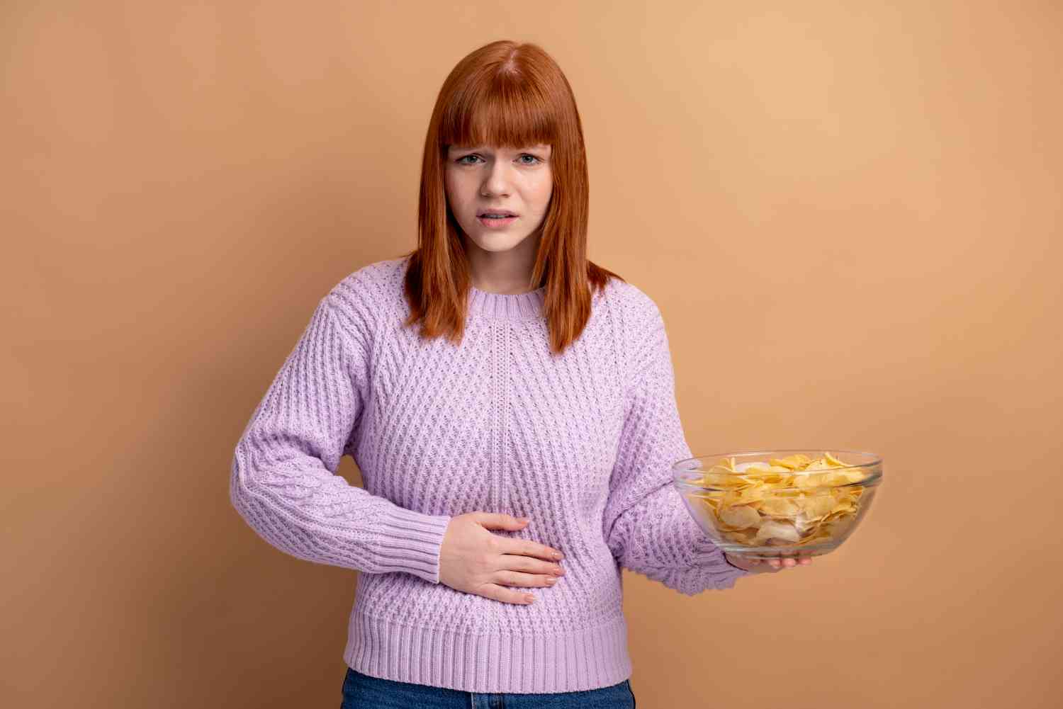 mujer sosteniendo bol de patatas fritas con dolor de estómago
