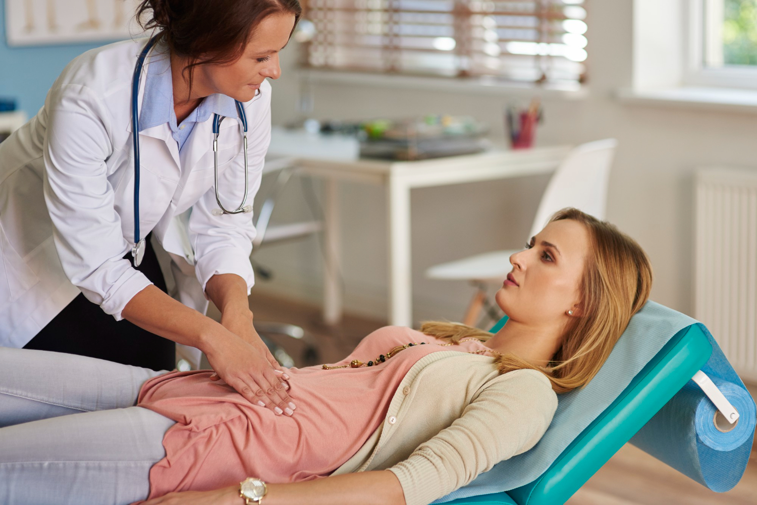 Doctora realizando exploración abdominal sobre paciente femenina que se encuentra en camilla.